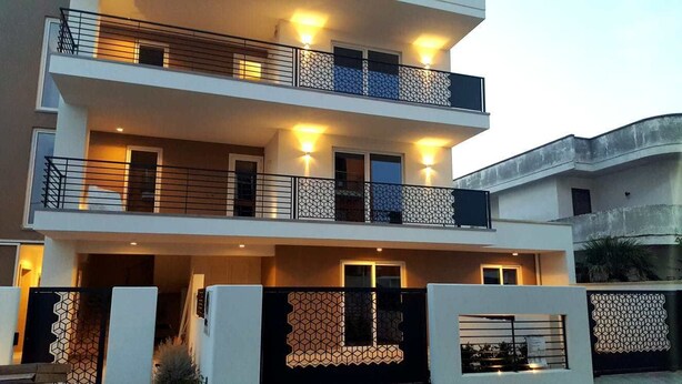 A modern two-story residential building with balconies, a geometric patterned fence, and a well-lit entrance. - Riva 33 (Porto Cesareo)
