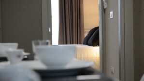 A hotel room with a bed, a bedside table with a cup and a bowl, and a door leading to another room. - Riva 33 (Porto Cesareo)