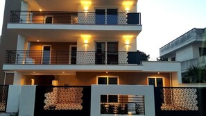 Un edificio residencial moderno de varios pisos con balcones, ventanas amplias y una valla con diseño geométrico.
