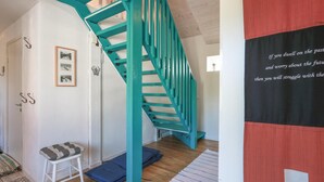 Eine Treppe mit türkisblauen Geländern, eine weiße Wand mit gerahmten Bildern, ein kleiner weißer Hocker und eine Wand mit rotem und schwarzem Text.
