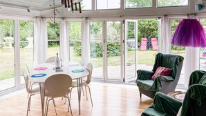 Ein Wintergarten mit Esstisch, Stühlen und einem grünen Sessel.