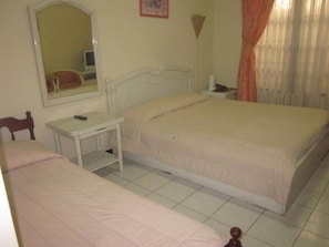 A bedroom with two beds, a bedside table, a mirror, and a window with curtains. - Hotel Vidi 1 (Depok)