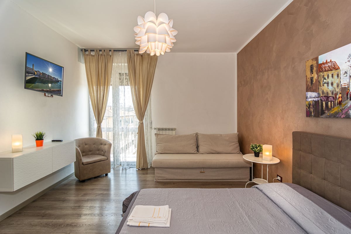 Una habitación de hotel moderna con una cama, un sofá, una silla, un televisor, una lámpara y un cuadro en la pared.