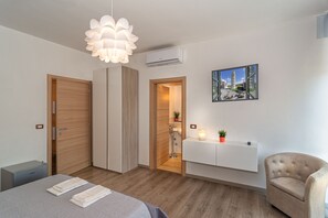 A modern bedroom with a bed, bedside tables, a chair, a pendant light, a radiator, and a painting of a cityscape. - La Candelaria (Pisa)