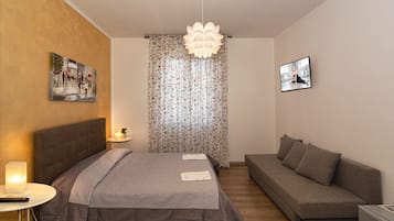 A bedroom with a bed, a sofa, a nightstand, a lamp, and a painting on the wall.