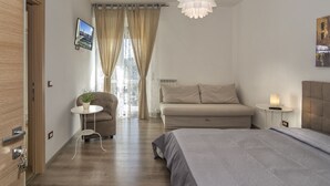 A modern bedroom with a bed, a sofa, a small table, and a hanging light fixture. - La Candelaria (Pisa)