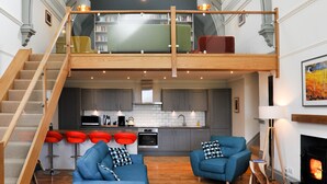 Ein großzügiges Loft mit hoher Decke, einer erhöhten Zwischenebene, einer Küchenzeile und einer Sitzecke mit Kamin.