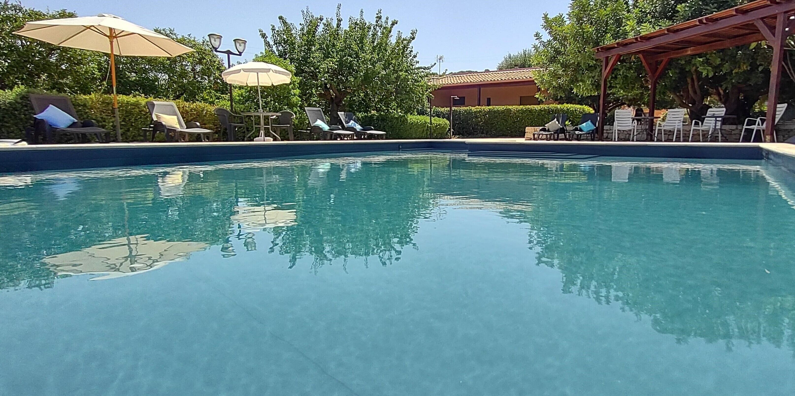A clear swimming pool with lounge chairs and umbrellas around it.