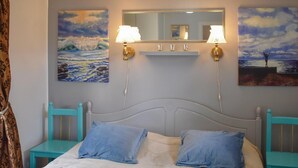 Ein Schlafzimmer mit einem Bett, zwei Nachttischen, einem Spiegel und Wandbildern mit Meerlandschaften.