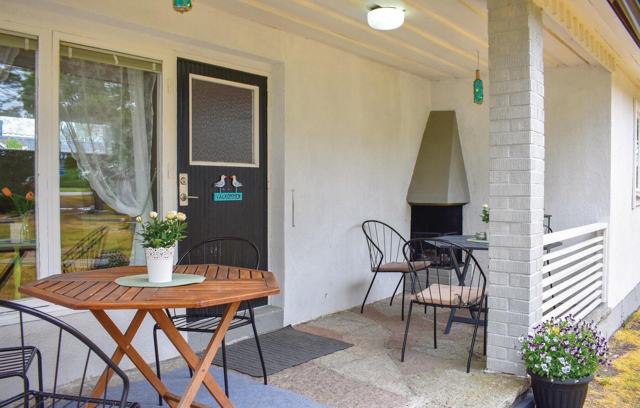 Une terrasse extérieure avec une table et des chaises en bois, un barbecue et une porte sur laquelle est affiché un panneau indiquant « Bienvenue ».