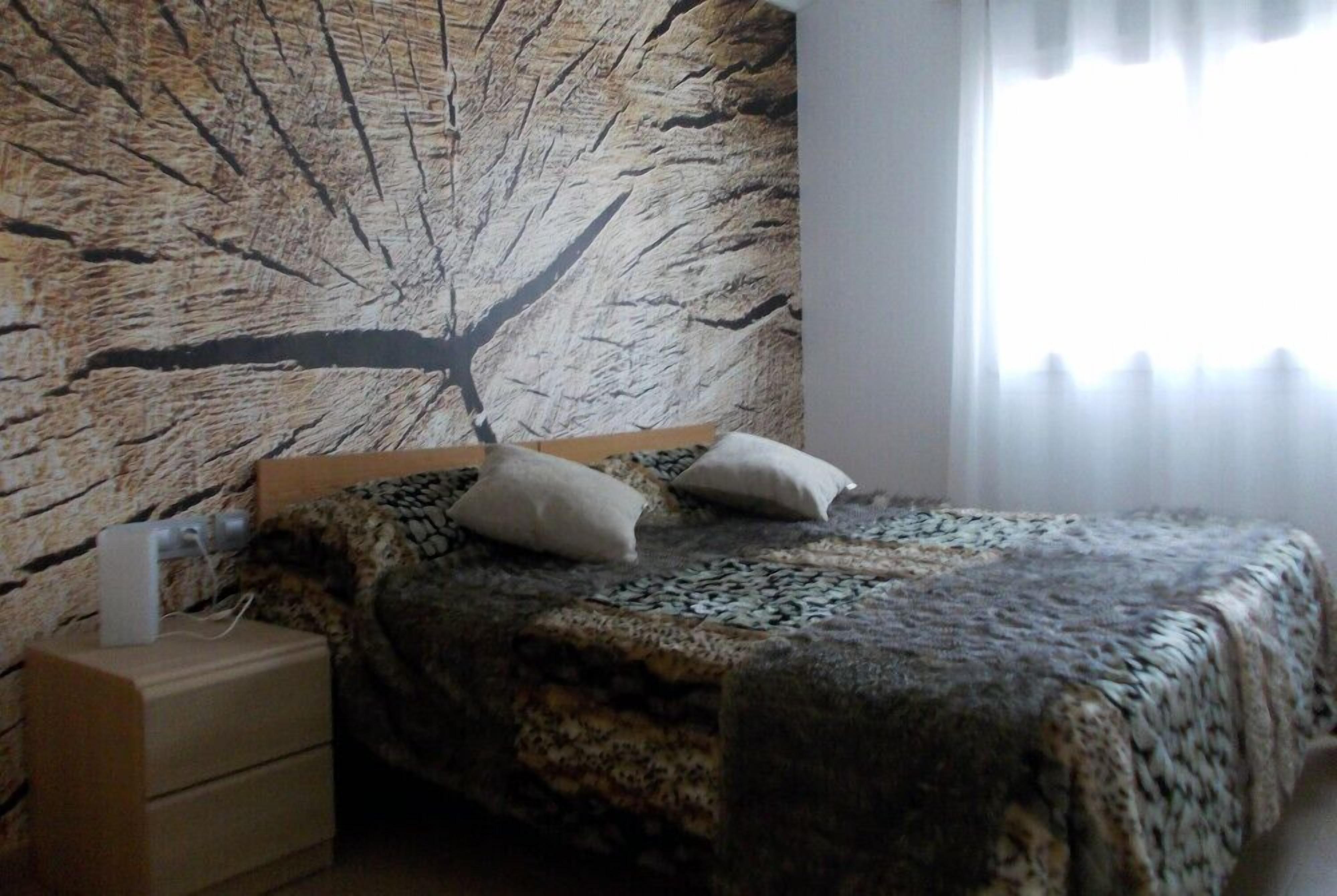 A bedroom with a bed, a nightstand, and a wall with a tree branch design.