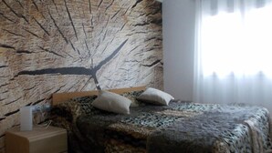 Une chambre à coucher avec un lit, une table de chevet et un mur décoré d’un motif représentant une branche d’arbre.