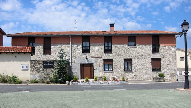 Un bâtiment à deux étages, doté d’une façade en pierre, d’un toit recouvert de tuiles et d’un petit jardin devant, agrémenté de fleurs.