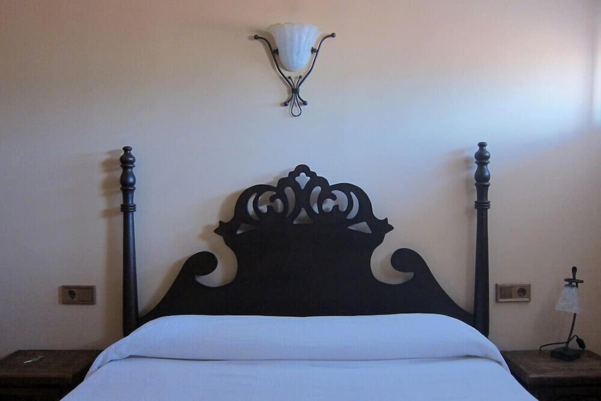 Un lit doté d’une tête de lit décorative, d’un luminaire fixé au mur et d’une petite table de chevet avec une lampe.