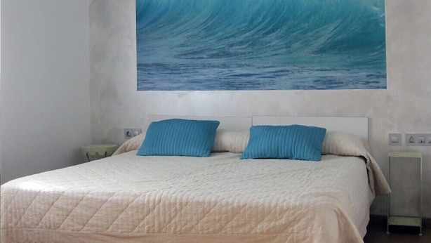 Une chambre à coucher avec un grand lit, deux oreillers, une table de chevet et une étagère fixée au mur.