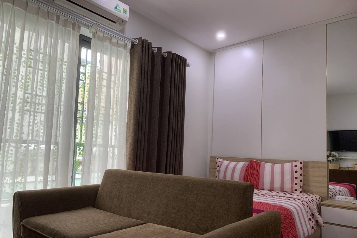 A bedroom with a sofa, a bed with striped bedding, a TV, and a wardrobe.