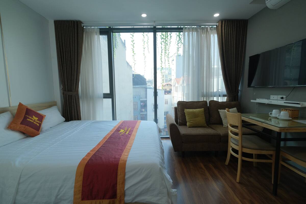 A hotel room with a large bed, a sofa, a dining table, and a TV.