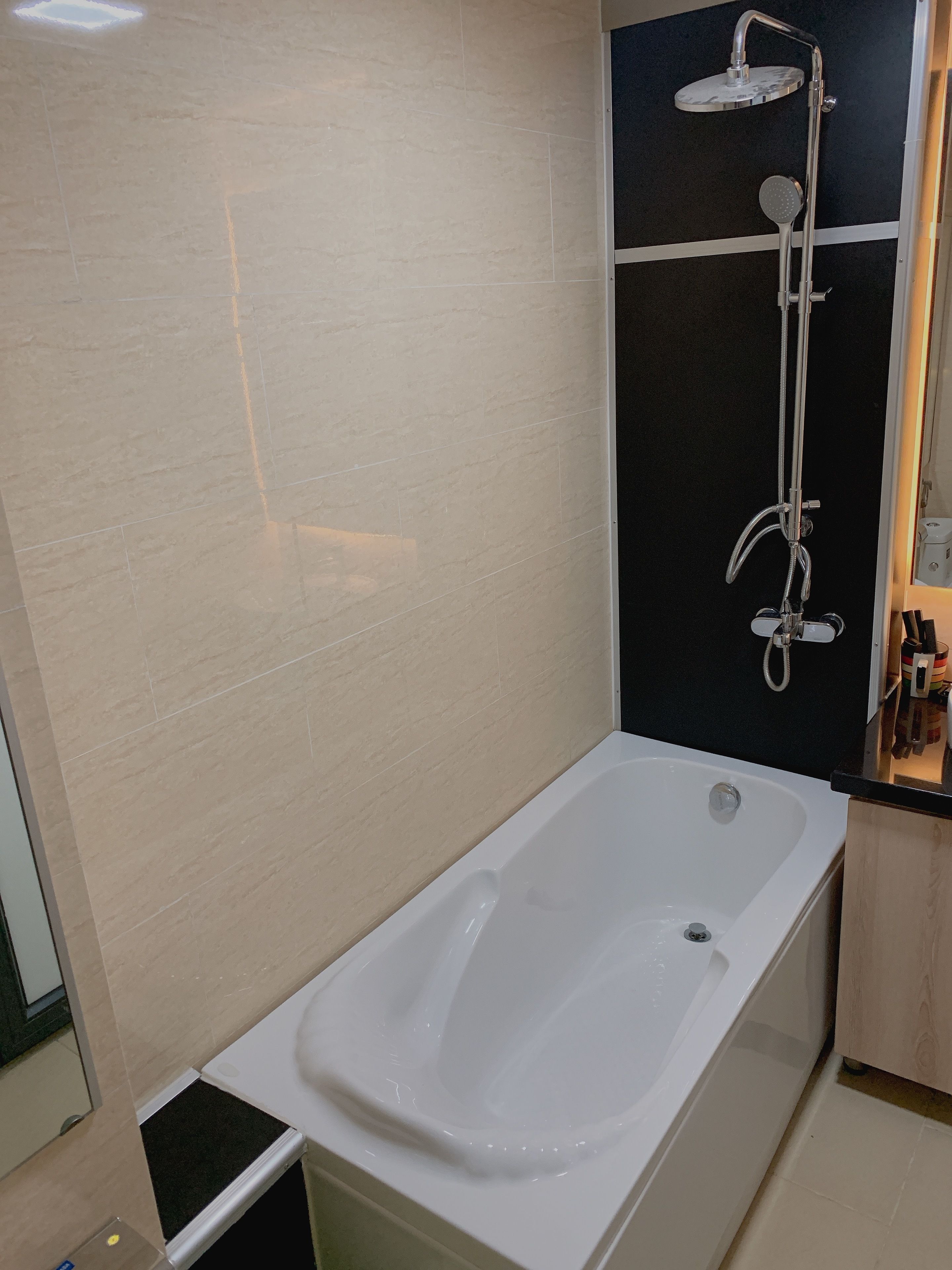 Une salle de bain moderne avec une baignoire blanche, un espace douche séparé et un mur recouvert de carreaux noirs.