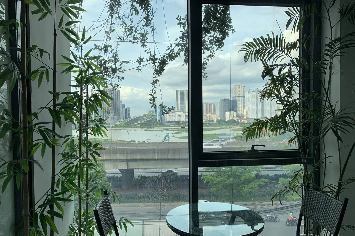 A room with a large window, a round glass table, two wicker chairs, and several potted plants.