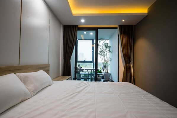 Habitación de hotel moderna con una cama grande, una mesita y un balcón con vistas.