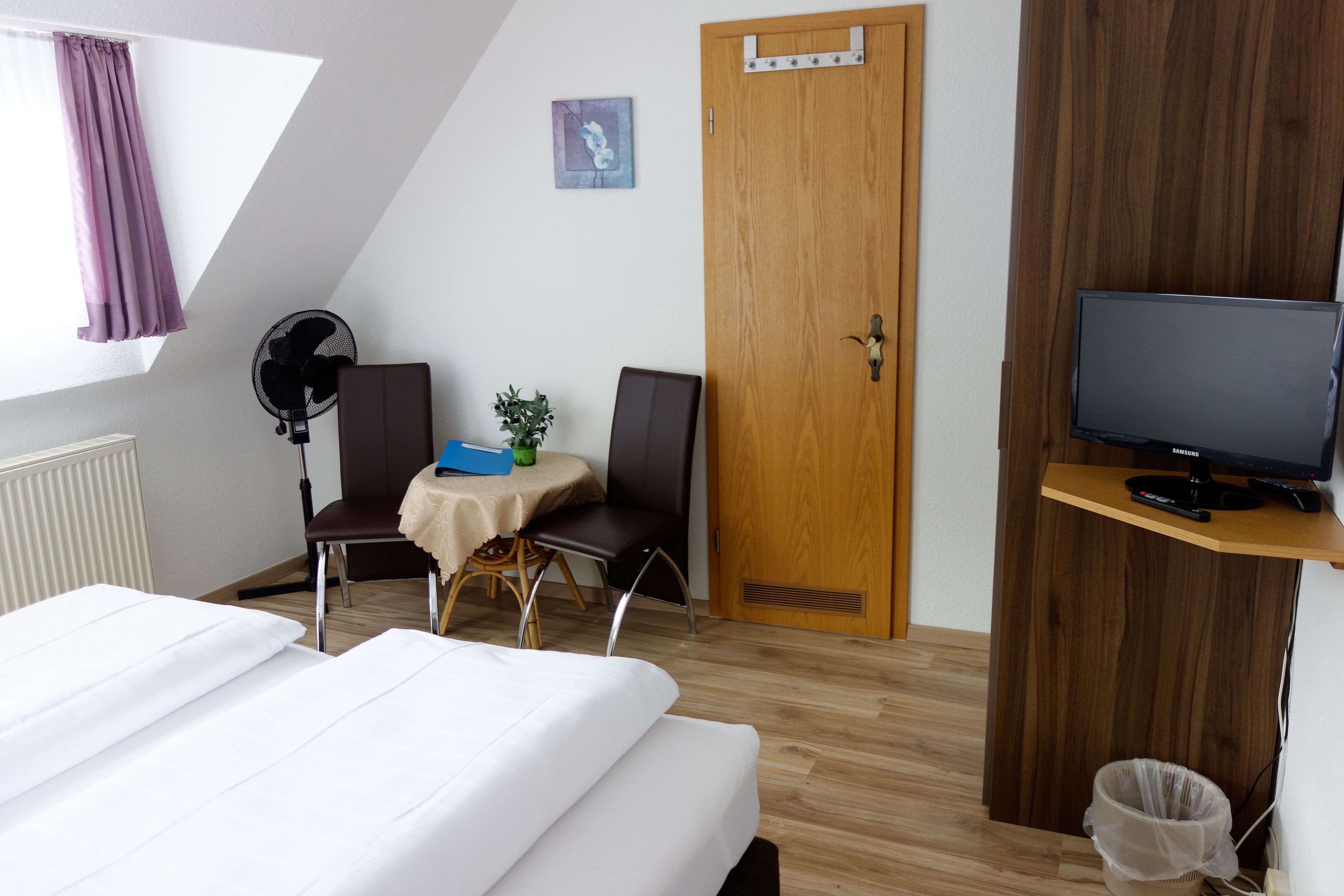 Une chambre d’hôtel comprenant un lit, un bureau avec une chaise, une télévision, une porte et une fenêtre avec des rideaux.