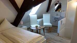 A modern, well-lit bedroom with a large bed, a small round table, and a chair. There is a skylight above the bed and a bathroom with a sink and mirror. - Hotel Haus Sonnschein (Cochem)