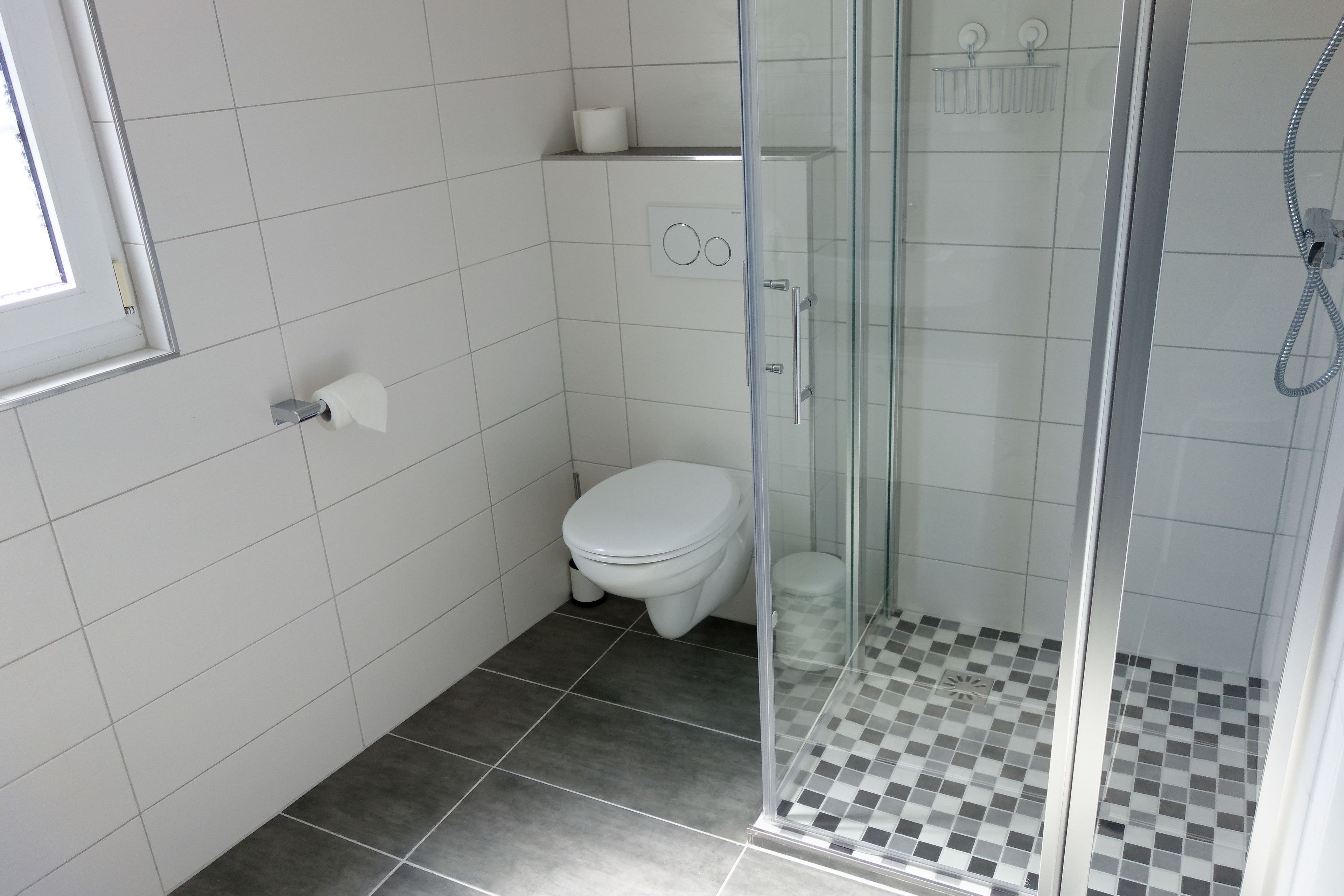 A bathroom with a toilet, a glass-enclosed shower, and a tiled floor.