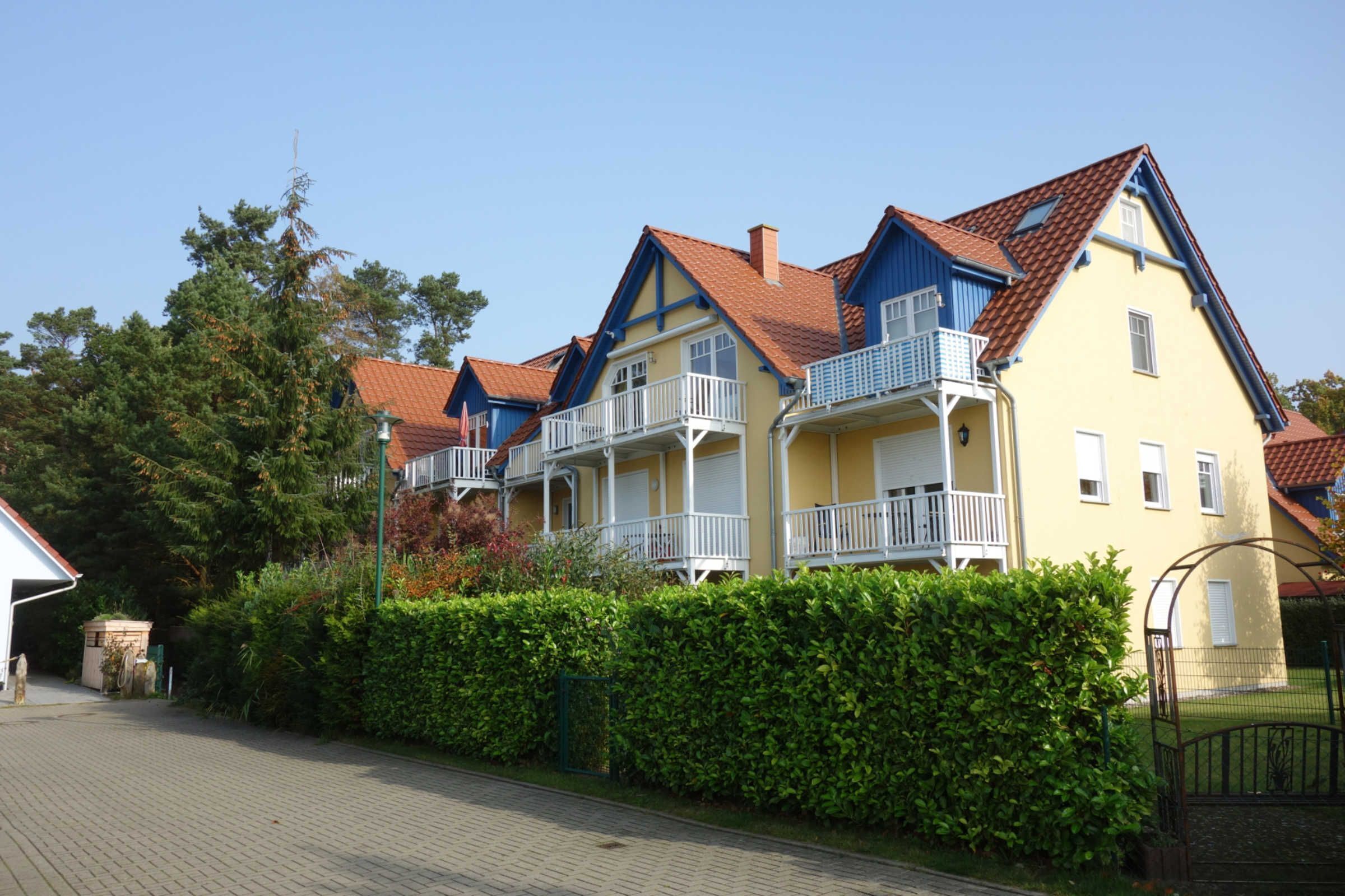 A row of yellow and blue houses with red roofs, white balconies, and a paved driveway.