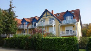 Una hilera de edificios de varios pisos en amarillo y azul con balcones, rodeados de vegetación.