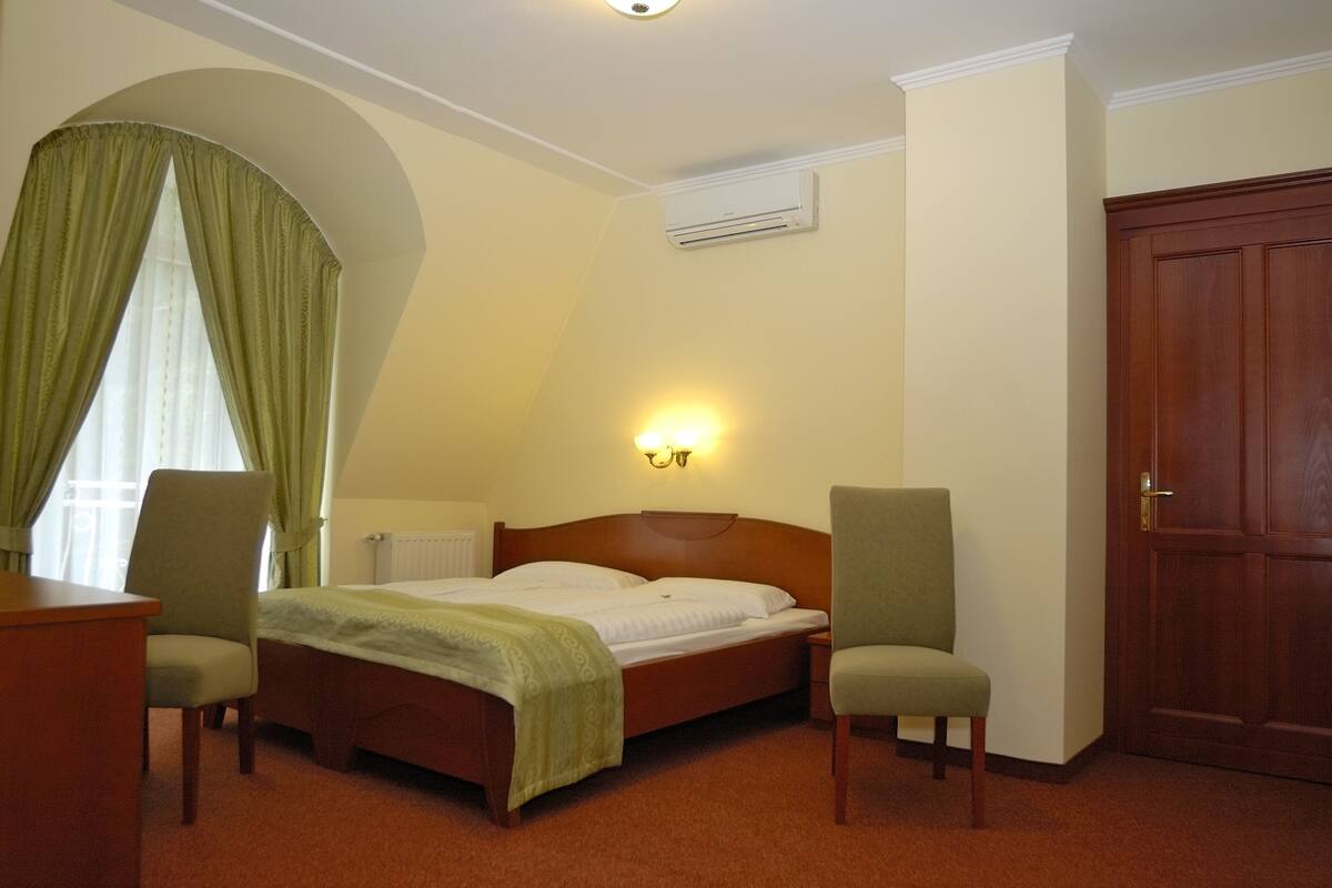 Ett hotellrum med en säng, två stolar, en garderob i trä och en väggmonterad luftkonditioneringsanläggning.