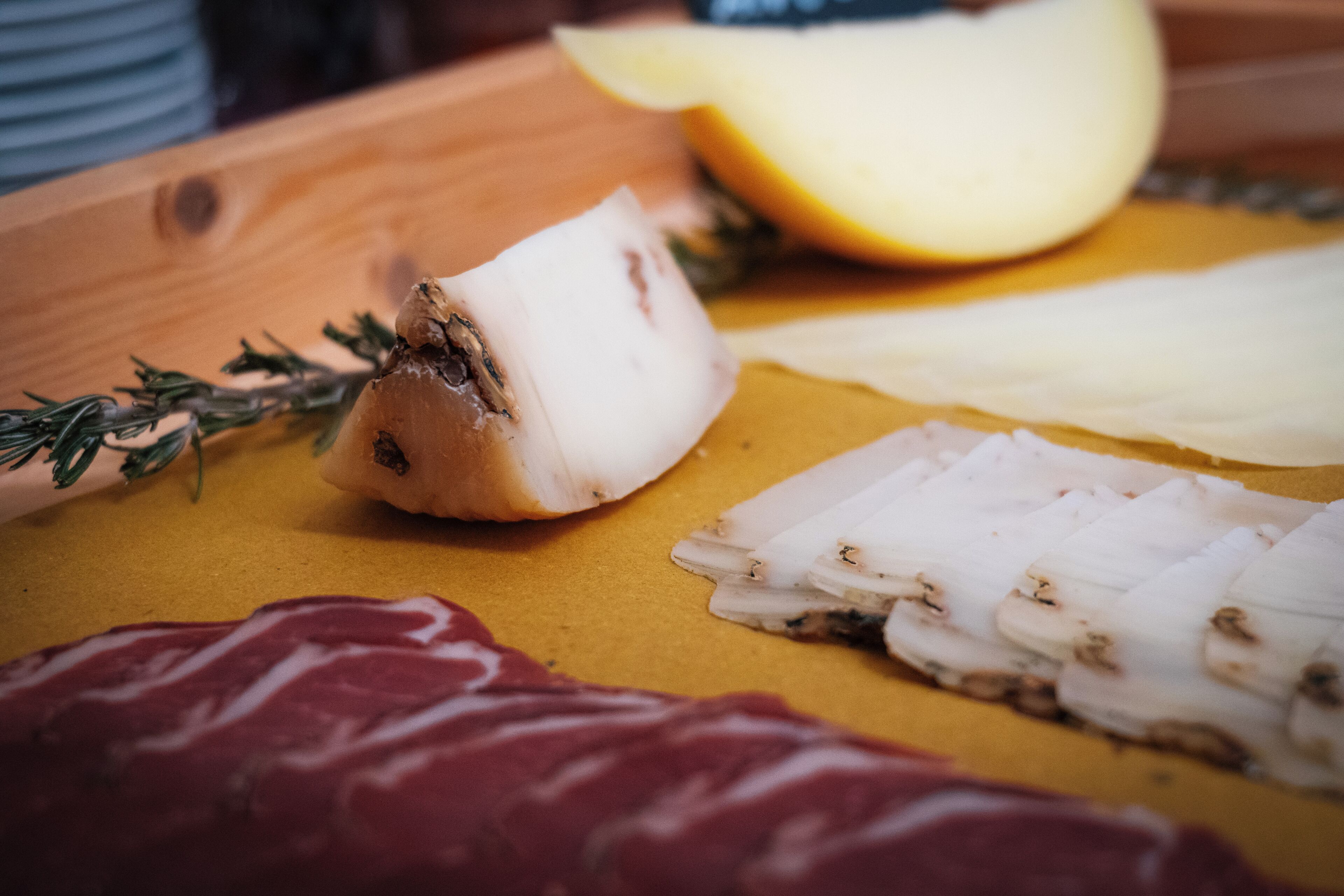 Una tabla de madera con diversos alimentos, incluyendo carne en rodajas, queso y hierbas aromáticas.