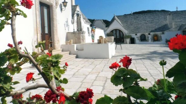 A courtyard with a white building featuring a wooden door and steps leading to a stone wall. - Masseria Pilano (Crispiano)