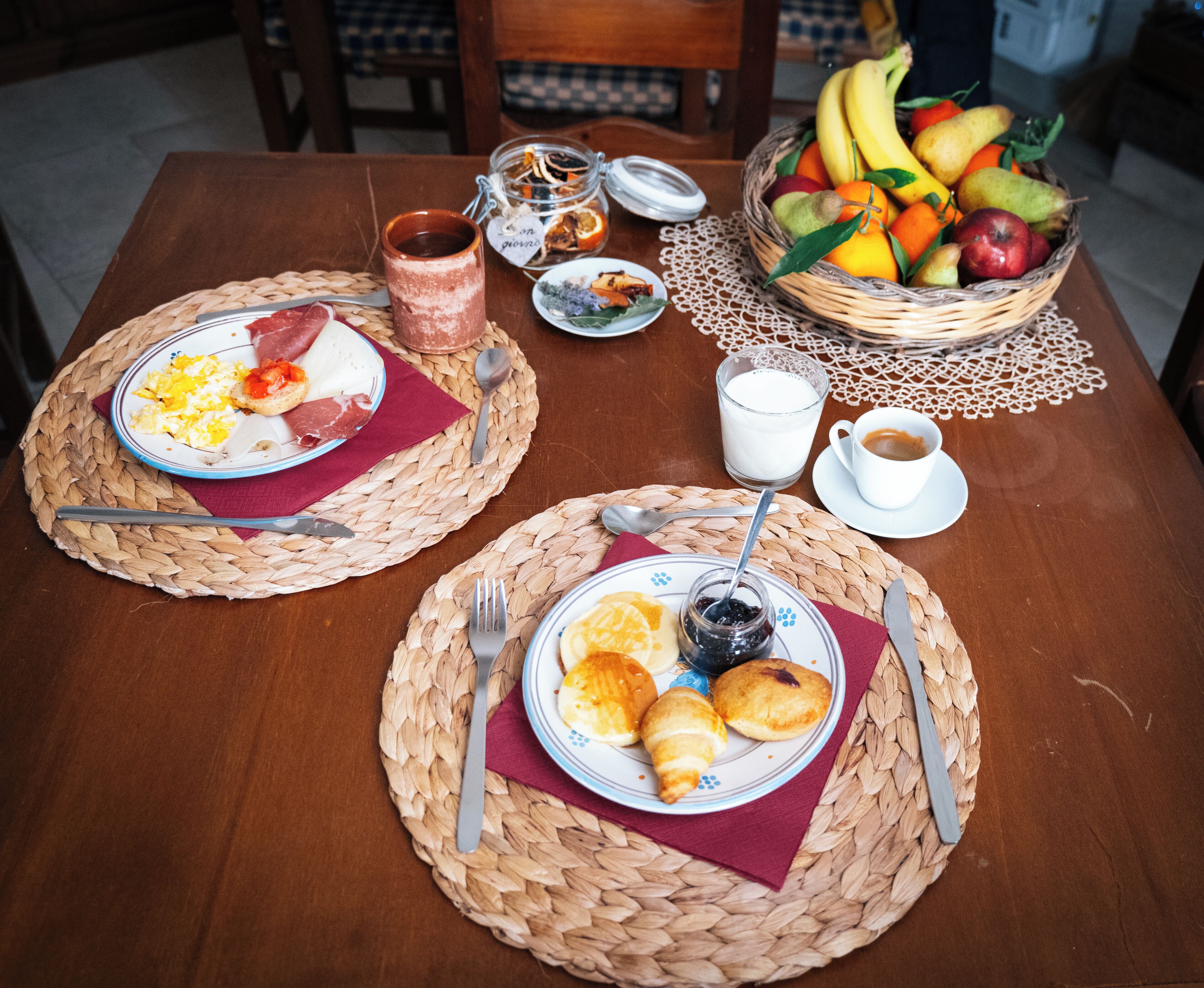 A breakfast setting with two plates of food, a fruit basket, and a glass of milk.
