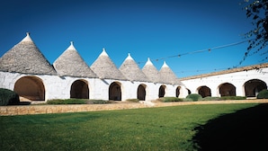 A row of white buildings with conical roofs and arched doorways, surrounded by a well-maintained lawn. - Masseria Pilano (Crispiano)