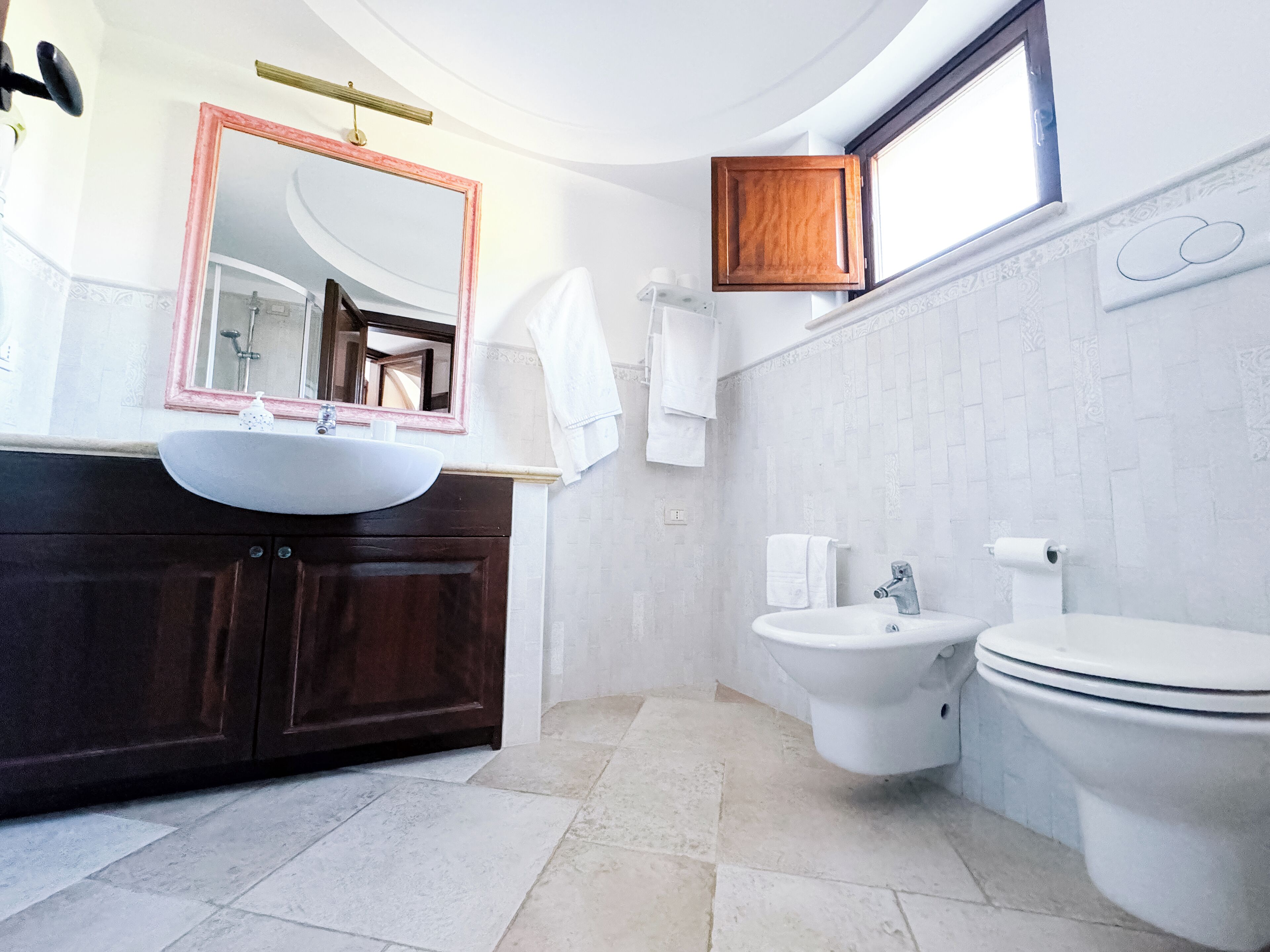 A modern bathroom with a round mirror, a sink, a bidet, and a toilet.