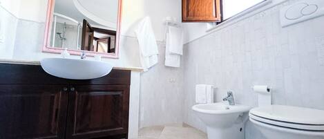 A modern bathroom with a round mirror, a sink, a bidet, and a toilet.