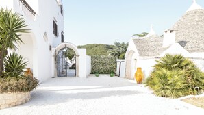A white building with an arched entrance, a stone wall, and a gate. - Masseria Pilano (Crispiano)