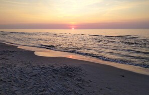 Ein Strand bei Sonnenuntergang, sanfte Wellen umspülen das Ufer.