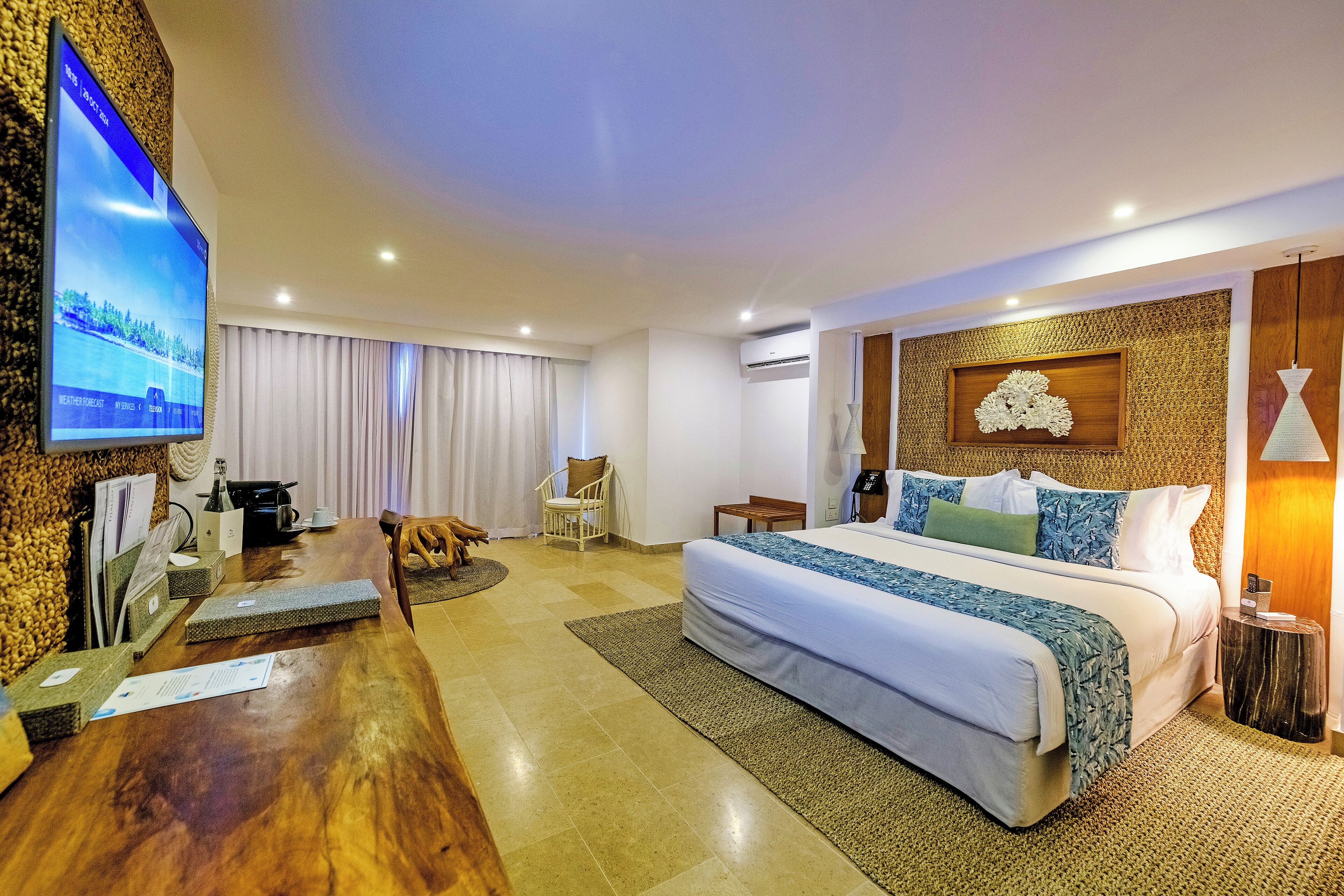 A hotel room with a large bed, a desk, a TV, and a wooden wall.