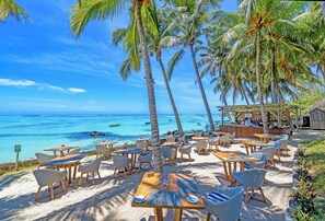A beachside restaurant with outdoor seating, palm trees, and a view of the ocean. - Seasense Boutique Hotel & Spa (Belle Mare)