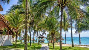 A pathway lined with palm trees leading to a beach with thatched umbrellas and a view of the ocean. - Seasense Boutique Hotel & Spa (Belle Mare)