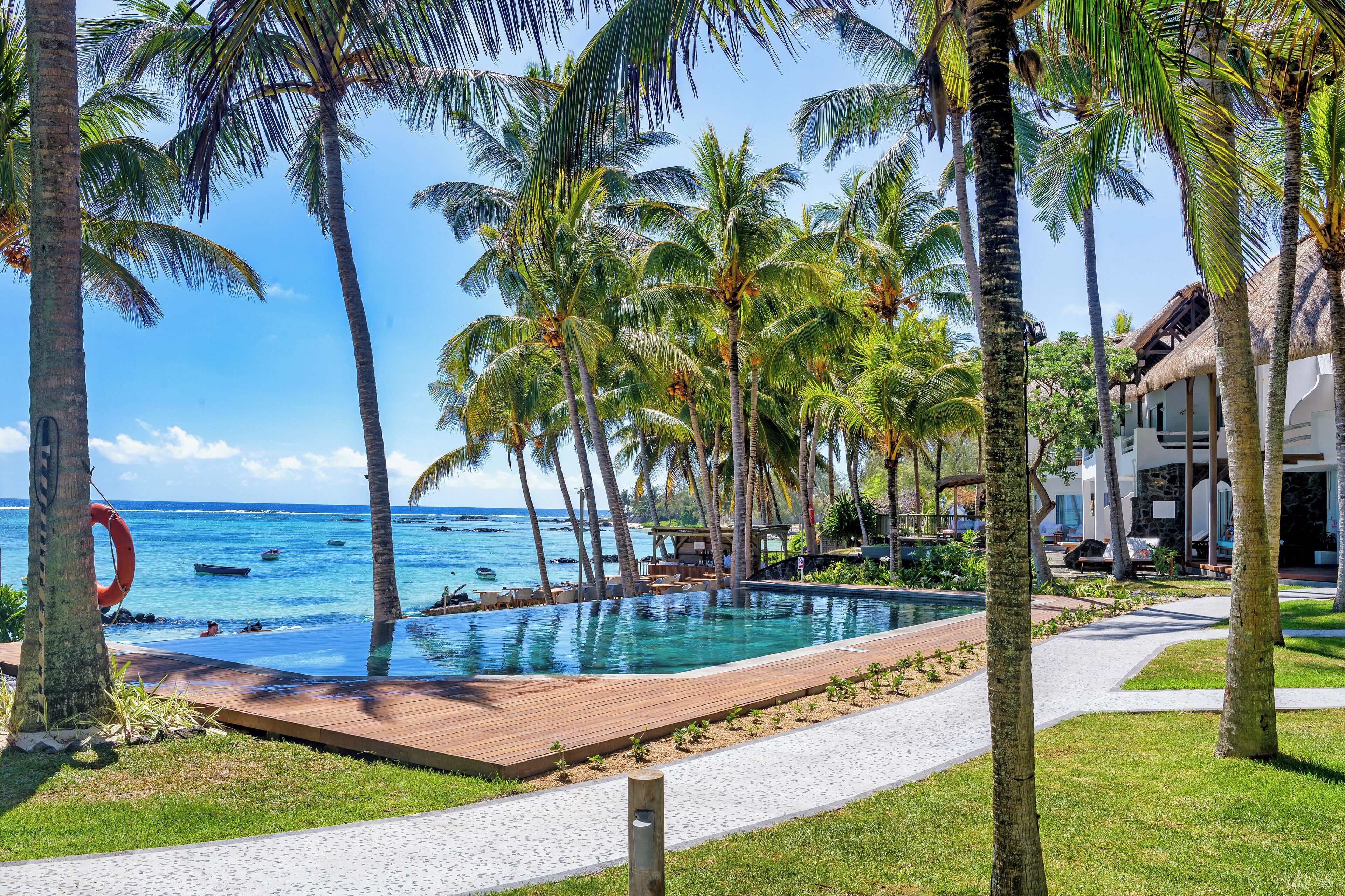 Un área de piscina con palmeras, una terraza de madera y vistas al océano.