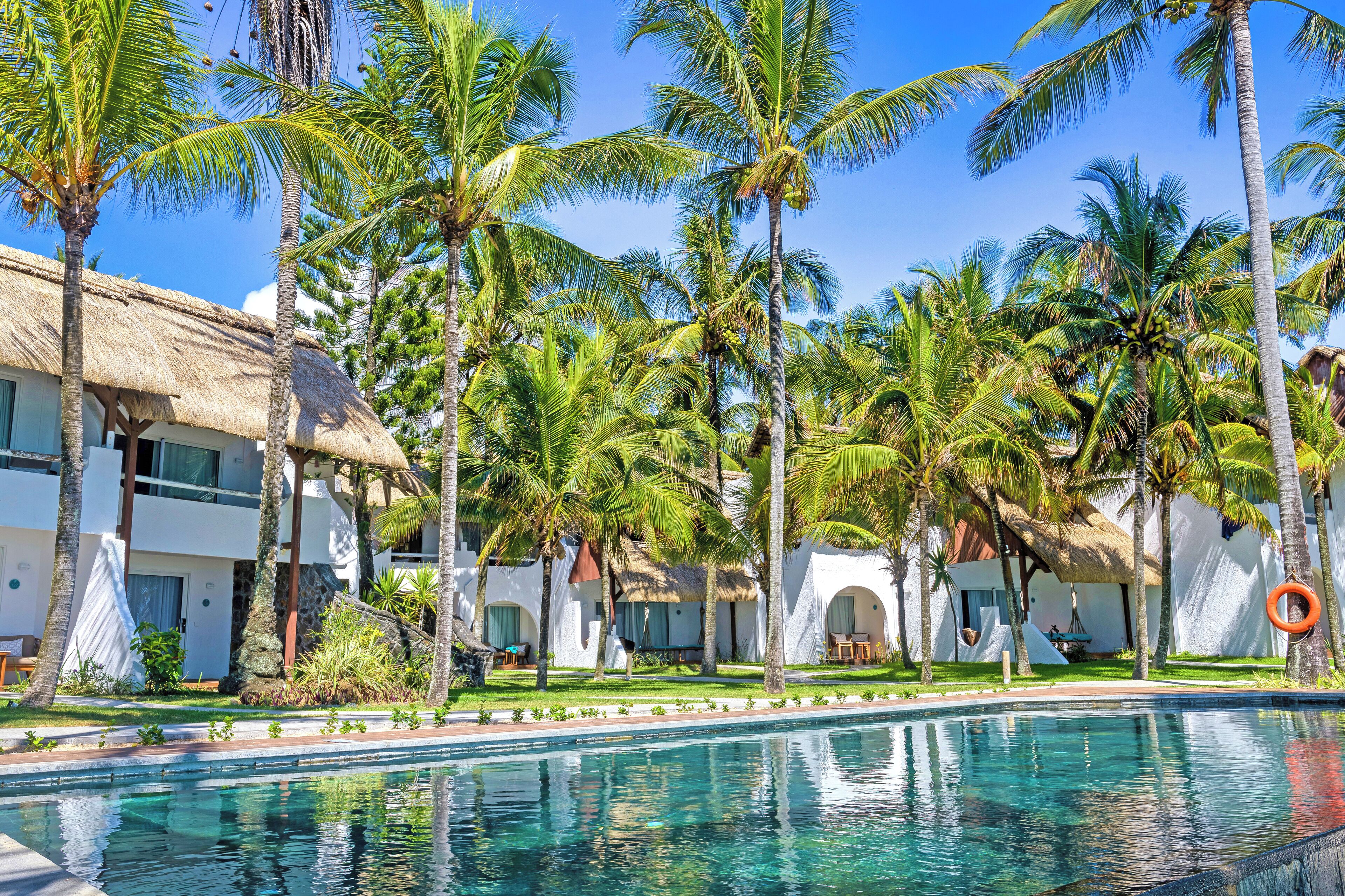 Resort com piscina, palmeiras e edifícios com telhado de palha.
