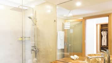 Un baño moderno con ducha de vidrio, tocador de madera y lavabo de mármol, y un espejo grande que refleja el ambiente.