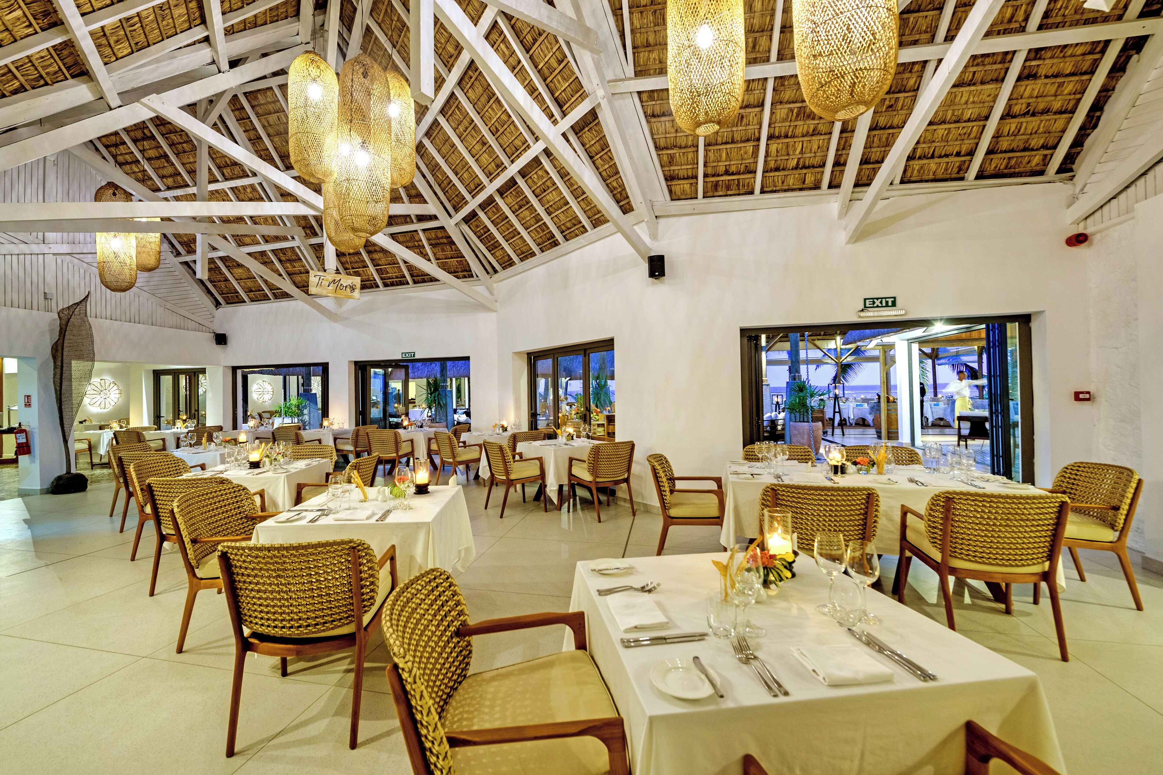 A spacious dining area with high ceilings and natural light, featuring wicker chairs and tables set for dining.