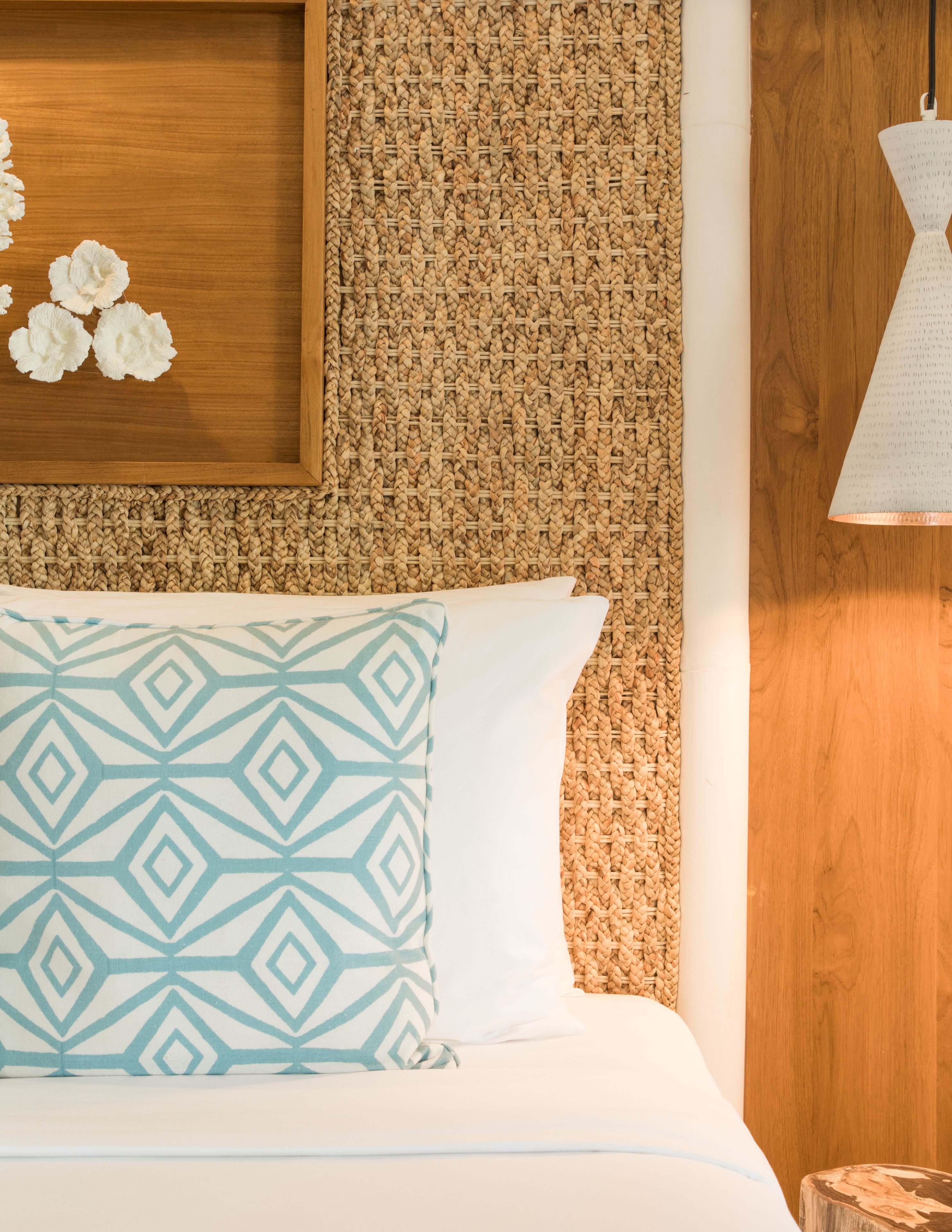 Una cama con un cojín estampado, un muro tejido y una lámpara colgante.