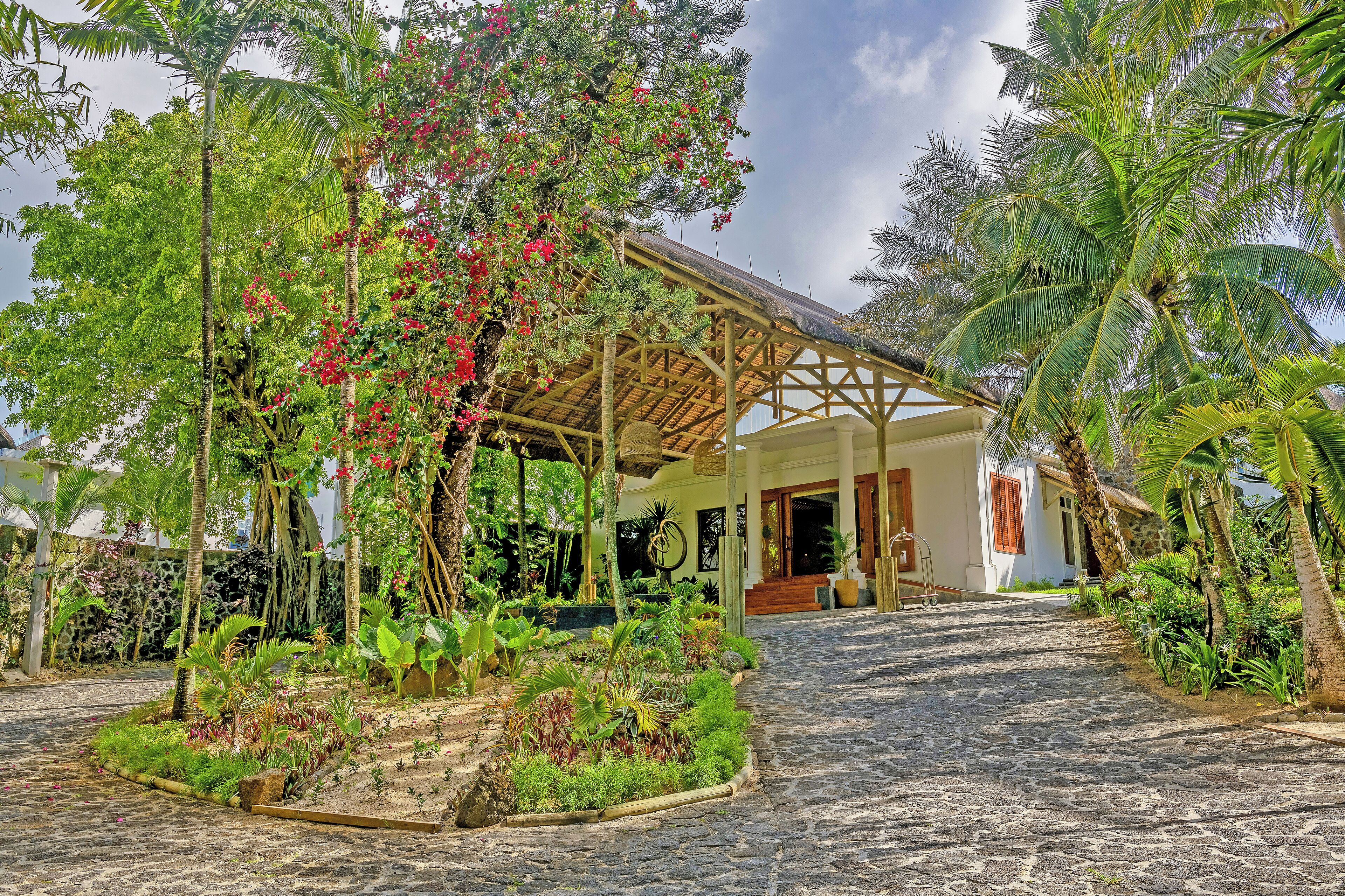 Un resort tropical con un sendero adoquinado que lleva a una estructura de madera con techo de paja.