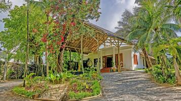 Un resort tropical con un sendero adoquinado que lleva a una estructura de madera con techo de paja.