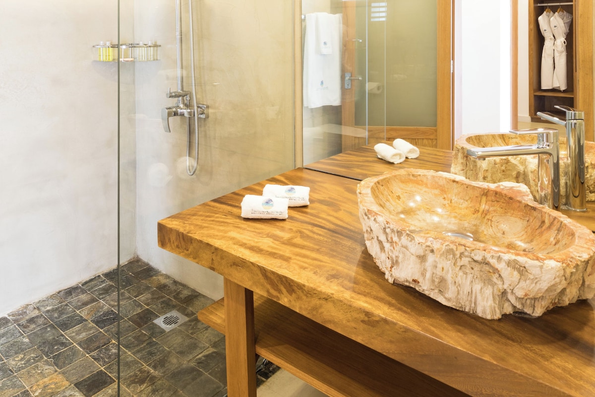 A modern bathroom with a glass-enclosed shower, a wooden vanity with a marble basin, and a large mirror reflecting the room.