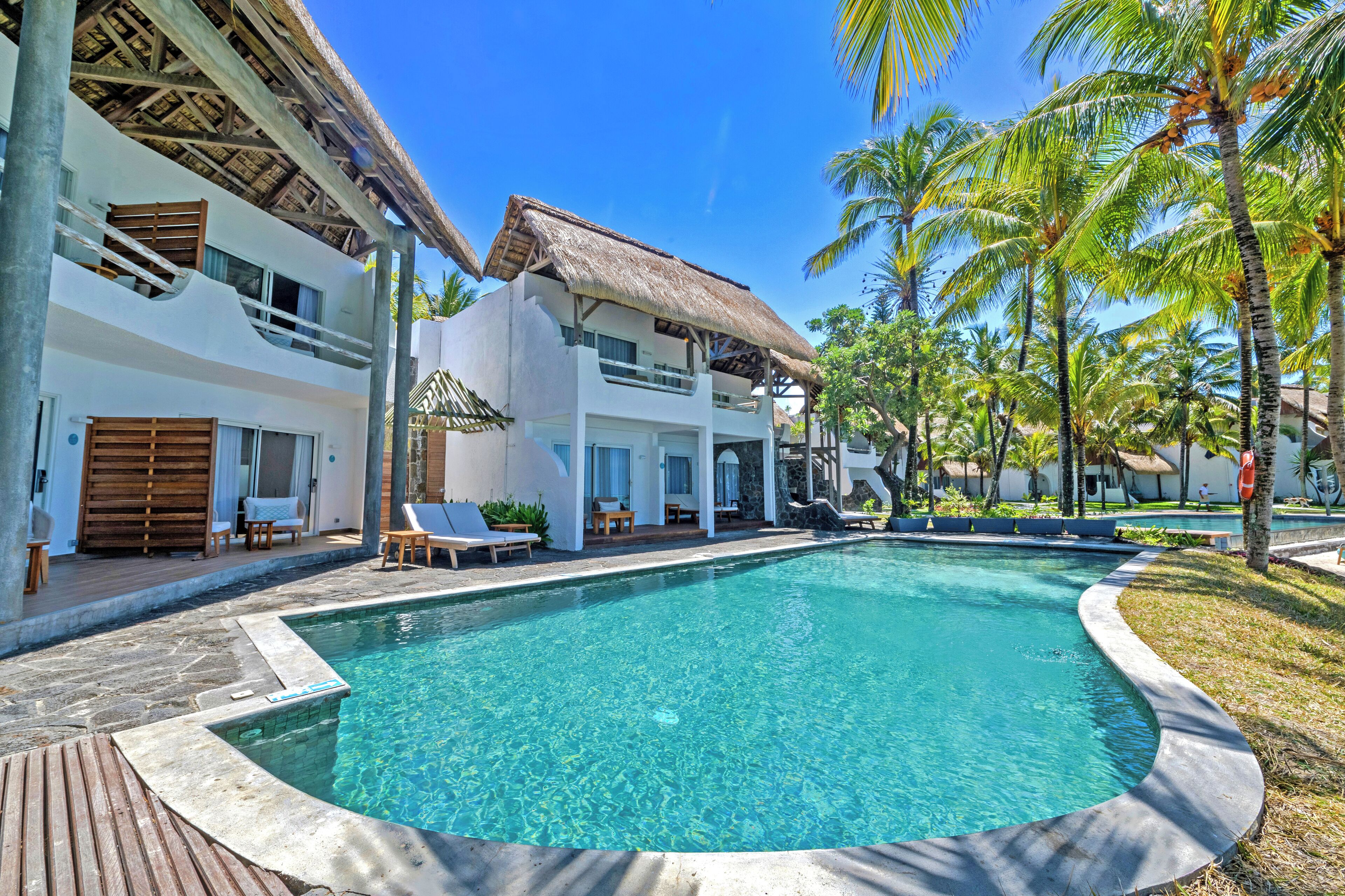 Ein Resort mit einem klaren Pool, Liegestühlen und Palmen.